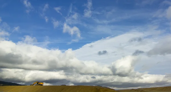 Lone excavator works on the horizon under the clouds — Stock Photo, Image