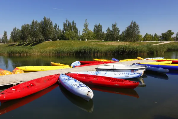 Boats and canoes made of many colors on a quiet lake with blue s — Stock Photo, Image