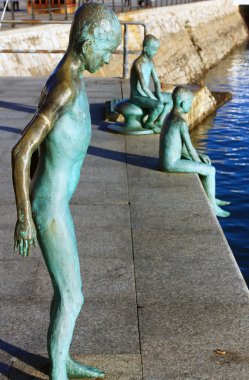 modern figures in bronze of child jumping into the sea from a pi clipart