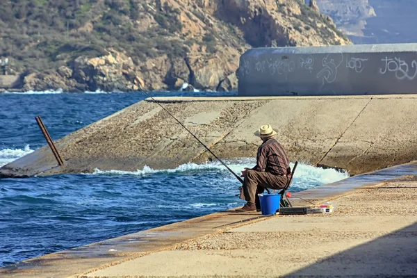 在海岸的一个拄着拐杖海钓鱼的老人 — 图库照片