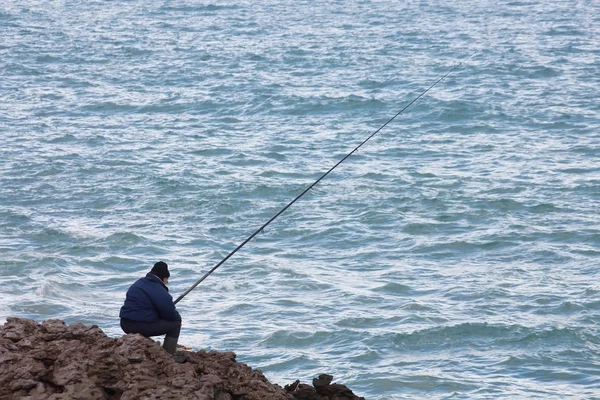 Homem mais velho pesca nas margens do mar com uma cana — Fotografia de Stock