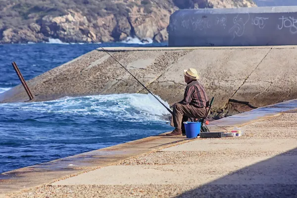 Homme plus âgé pêche sur les rives de la mer avec une canne — Photo