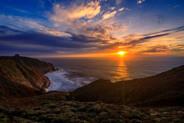 Kaliforniya 'daki Devil' s Slide yolunda engebeli uçurumlar, günbatımında bir güneş doğumu ve arka planda uzun süre kalmaktan Pasifik Okyanusu 'nun ipeksi suları.