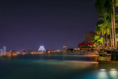 Singapur - 07 Eylül 2019: Marina Bay Sands lüks otelinde ve şehir siluetinde günbatımında gökdelenlerle ünlü sonsuz sörf tahtası havuzu