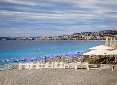 Akdeniz 'in Nice' teki turkuaz suyu, Fransa 'nın Cote d' Azur şehrinde sahil şemsiyeleri ve sandalyeli çakıl taşı plajı.