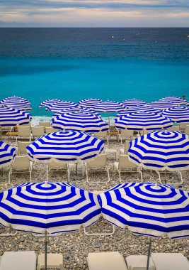 Pebble beach along Promenade des Anglais with beach umbrellas and chairs with the turquoise water of the Mediterranean Sea in Nice, Cote d'Azur France