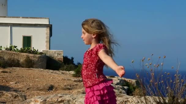 Glückliches kleines blondes Mädchen spürt Wind im hohen Leuchtturm-Meer — Stockvideo