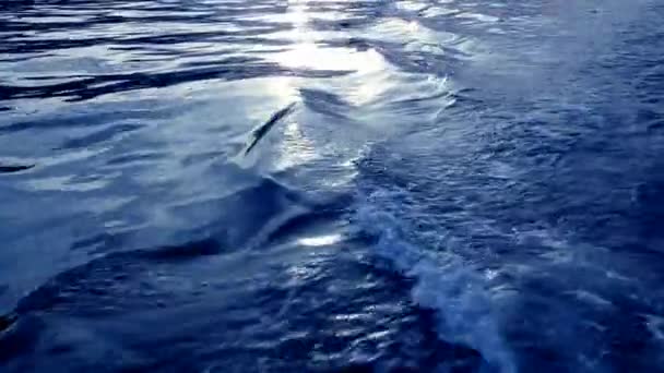 Água do mar azul com reflexos vermelhos do pôr do sol vista de um barco em movimento — Vídeo de Stock