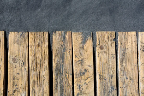 Black beach sand and wooden floor — Stock Photo, Image