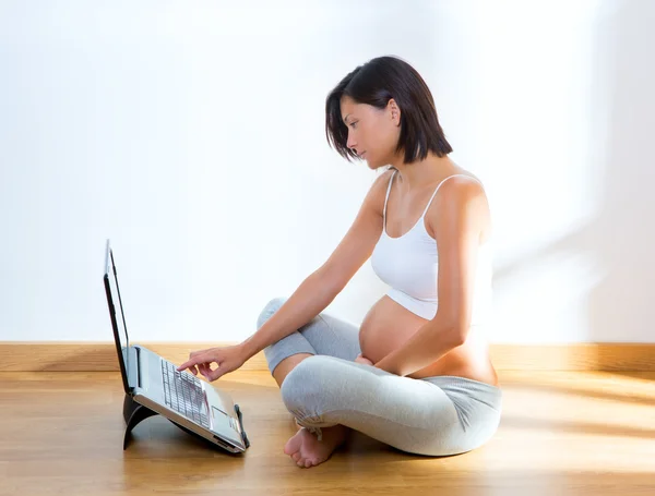 Bella donna incinta a casa con computer portatile — Foto Stock