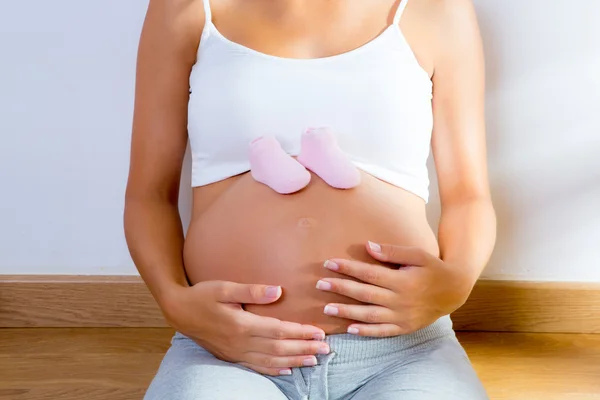 Mulher grávida bonita com sapatos de bebê na barriga — Fotografia de Stock