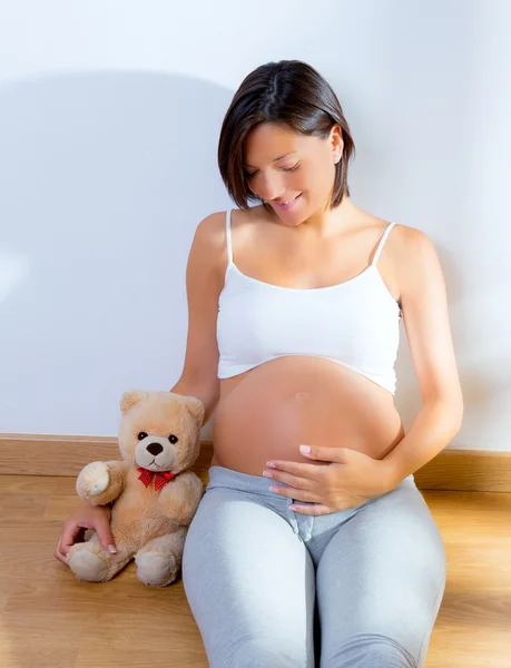 Mujer embarazada sentada en el suelo con oso de peluche — Foto de Stock
