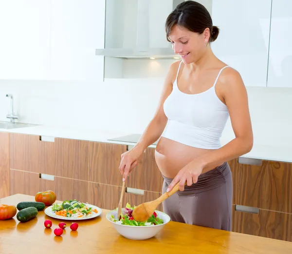 Beautiful pregnant woman at kitchen preparing salad — Stock Photo, Image