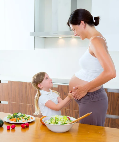 Hermosa madre embarazada con su hija en la cocina —  Fotos de Stock