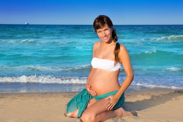 Mooie zwangere vrouw op knieën op blauwe strand — Stockfoto