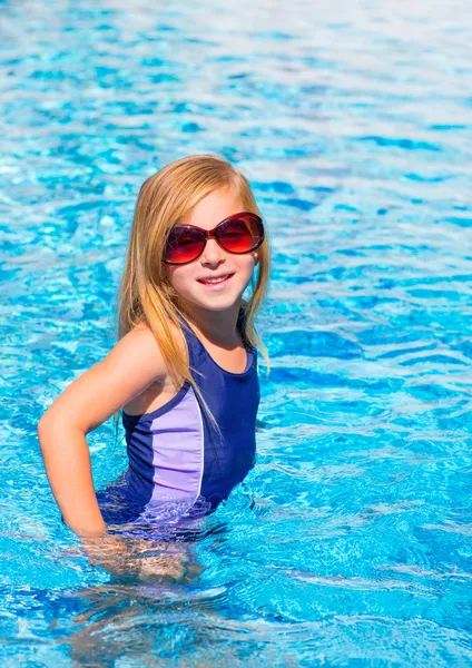 Menina loira na piscina azul posando com óculos de sol — Fotografia de Stock