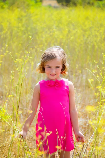 Kind kind meisje in voorjaar gele bloemen veld en roze jurk — Stockfoto