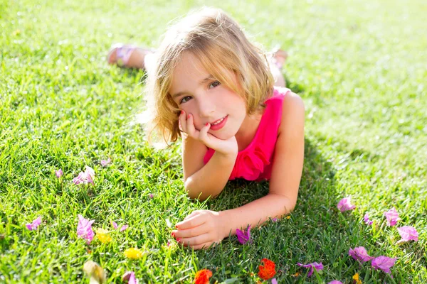 Blond liten tjej ligga avslappnad i trädgård gräs med blommor — Stockfoto