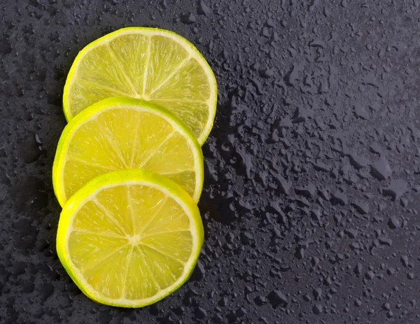 Fresh lima slices with water drops on black — Stock Photo, Image