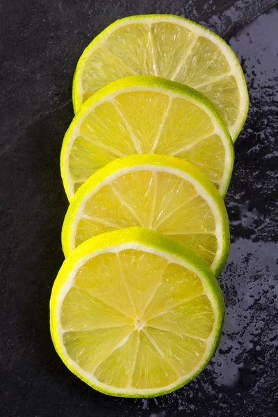 Fresh lima slices with water drops on black — Stock Photo, Image