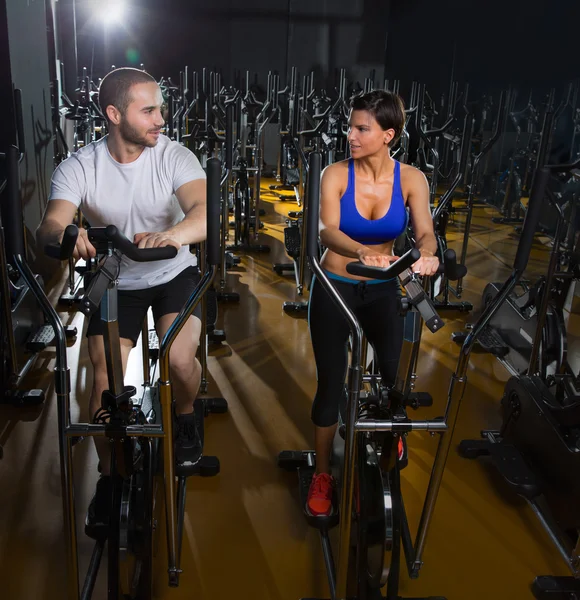 Elliptical walker trainer man and woman at black gym — Stockfoto