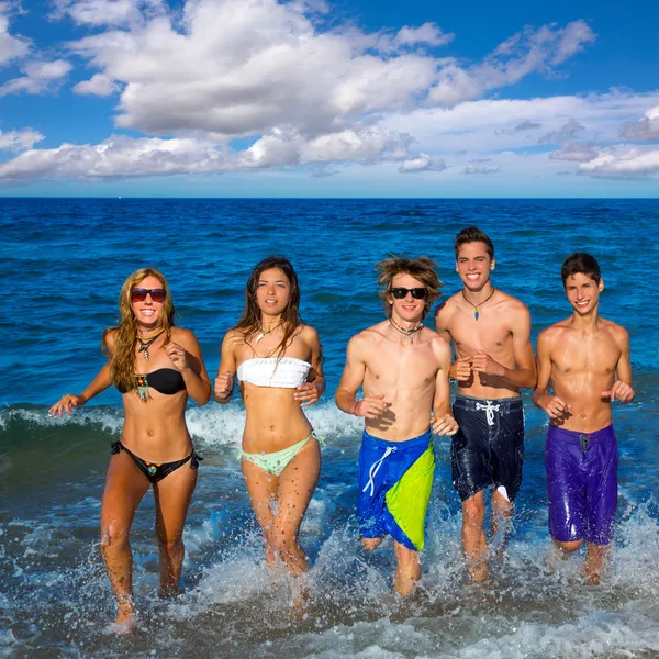 Adolescentes grupo correndo feliz espirrando na praia — Fotografia de Stock