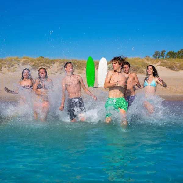 Adolescentes surfistas grupo correndo praia espirrando — Fotografia de Stock
