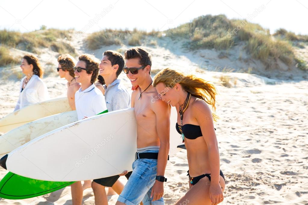 Surfer teen boys and girls group walking on beach