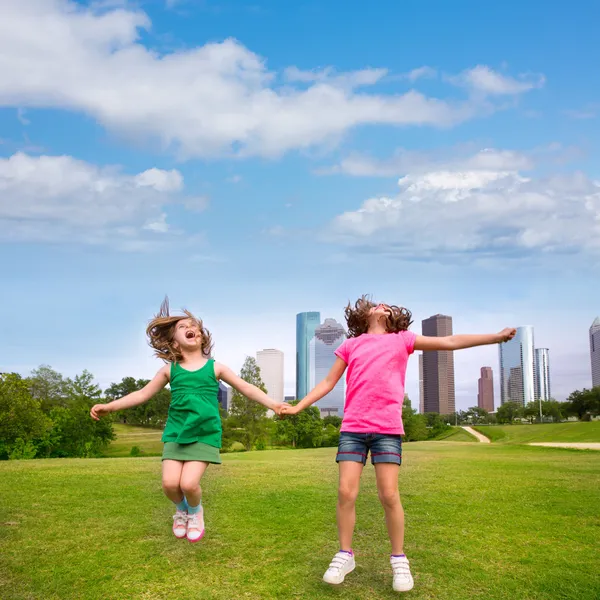 Two girls friends jumping happy holding hand in city skyline — Stock Photo, Image