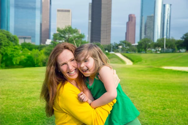 Madre e hija feliz abrazo riendo en parque en horizonte de la ciudad —  Fotos de Stock