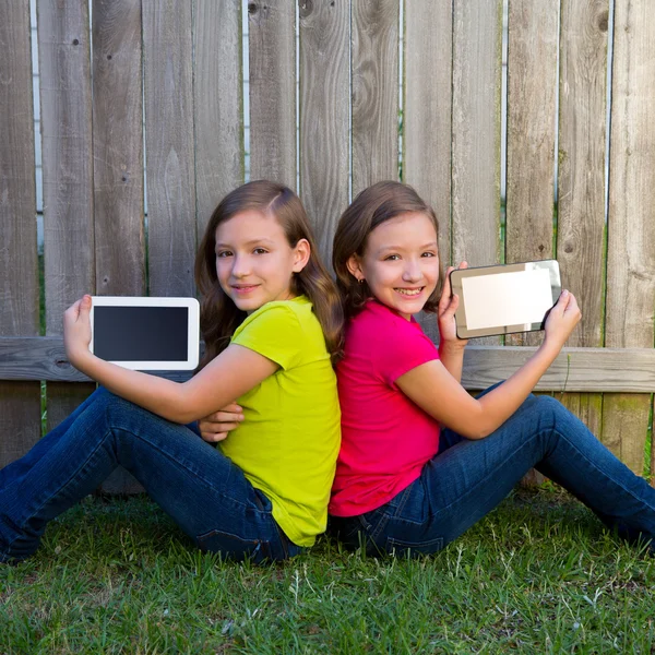 Tvillingsyster flickor leker tablet pc sitter på bakgården gräsmatta — Stockfoto