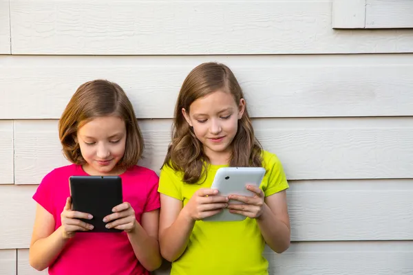 Tvillingsyster flickor leker med tablet pc glad på vit vägg — Stockfoto