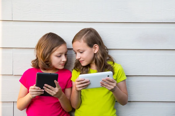 Tvillingsyster flickor leker med tablet pc glad på vit vägg — Stockfoto