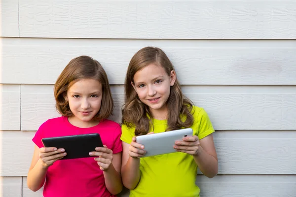 Tvillingsyster flickor leker med tablet pc glad på vit vägg — Stockfoto