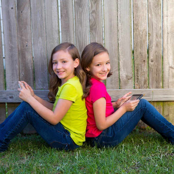 Dvojče dívky hrají počítače tablet pc sedí na zahradě trávník — Stock fotografie
