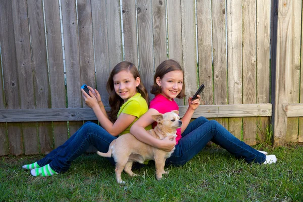 Tweelingzus meisjes spelen smartphone en chihuahua hond — Stockfoto