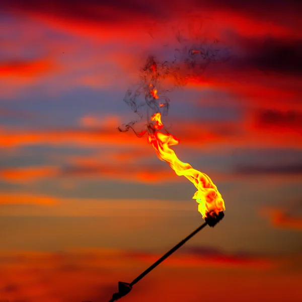 Fire torch at sunset sky with red clouds — Stock Photo, Image