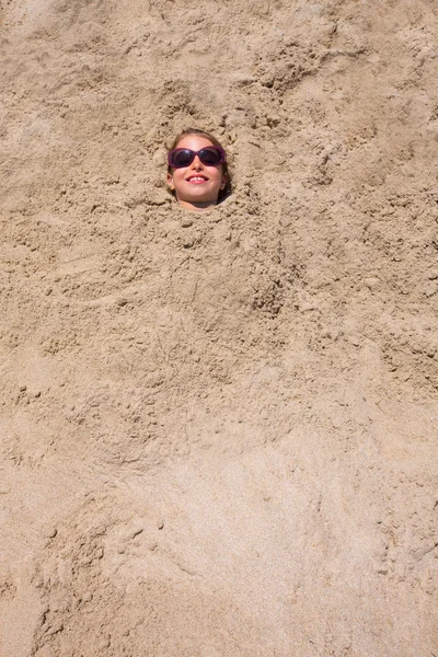 Rolig tjej spelar begravd i sandstrand leende solglasögon — Stockfoto