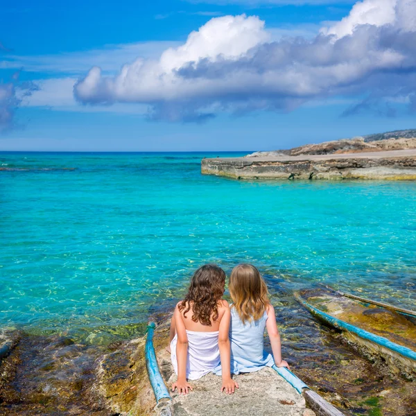 Blond och brunett kid flickorna sitter på stranden port — Stockfoto