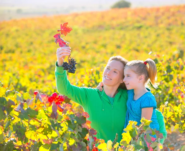 Madre e hija en el viñedo de otoño sonriendo sosteniendo la uva — Foto de Stock