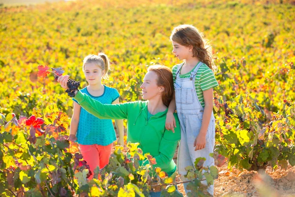 Mother and daughters on autumn vineyard smiling holding grape — Stock Photo, Image