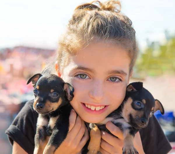 Девочка играет с щенячьими собаками улыбаясь — стоковое фото