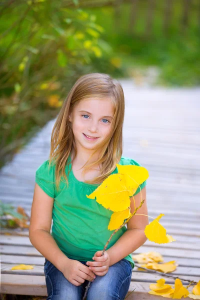 Kluk holka v podzimní dřevěné paluby se žlutými listy venkovní — Stock fotografie
