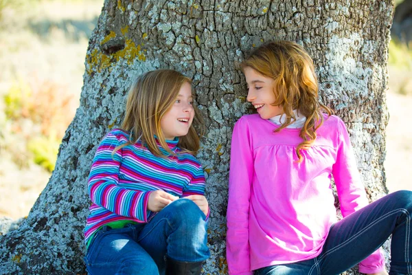 Hermana niña niñas sonriendo sentarse relajado en un tronco de roble —  Fotos de Stock