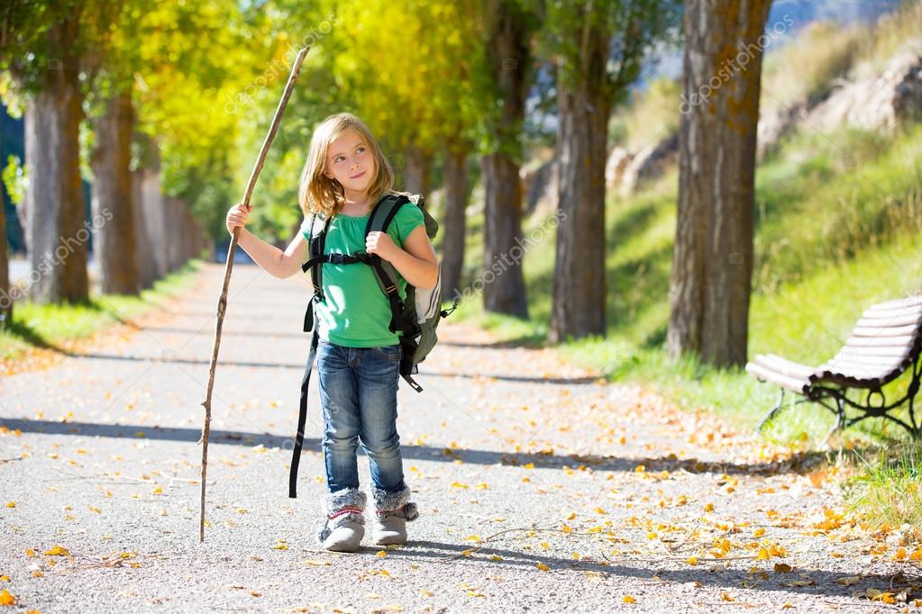 Blond explorer kid girl walking with backpack in autumn trees