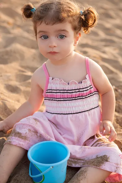 Blu eyes brunette toddler girl playing with sand in beach — Stock Photo, Image