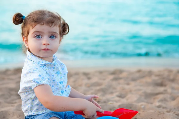 Blu eyes brunette toddler girl playing with sand in beach — Stock Photo, Image