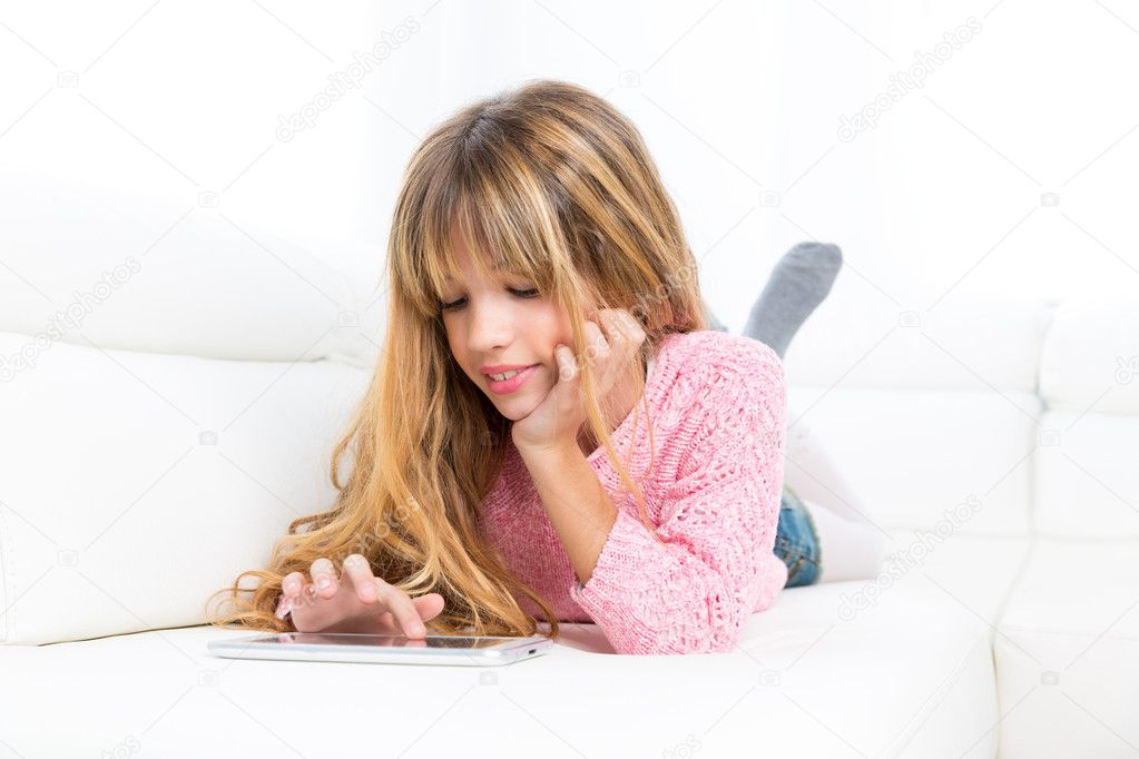 Blond kid girl playing with tablet pc on white sofa