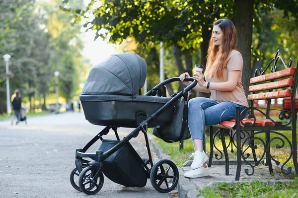 Annem bankta oturuyor. Bebek arabasında oturan bir kadın bebeğini itiyor. Aile kavramı.