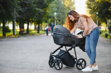güzel ve genç kadın anne ve Bebek arabasındaki bebek parkta yürüyüş